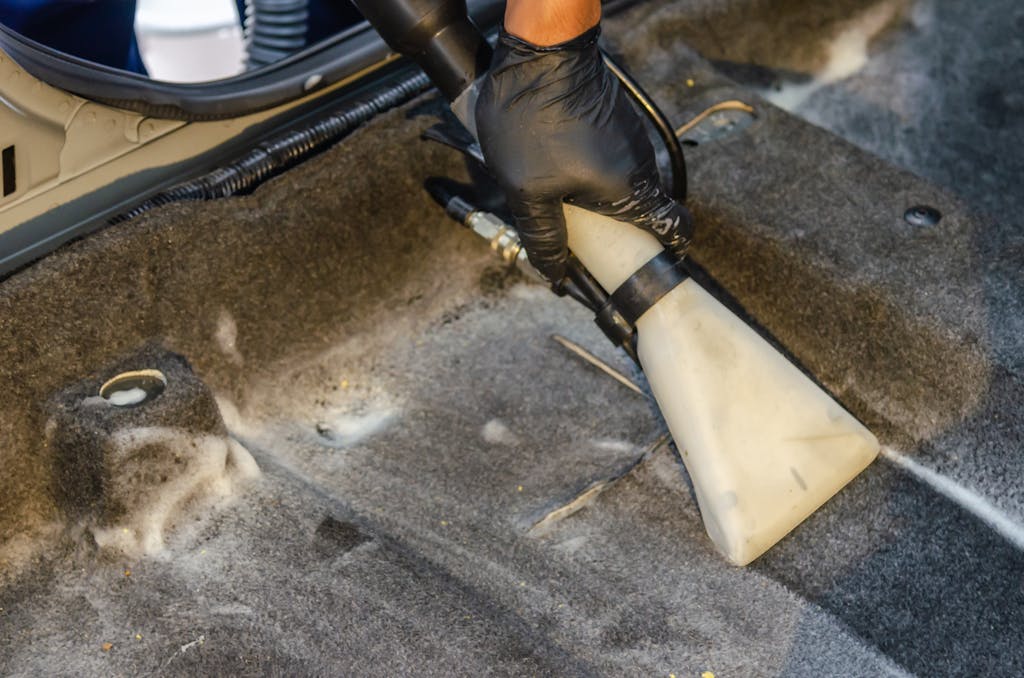 St. Augustine 8 A hand in a glove using a vacuum to clean a car interior carpet, removing dirt effectively.