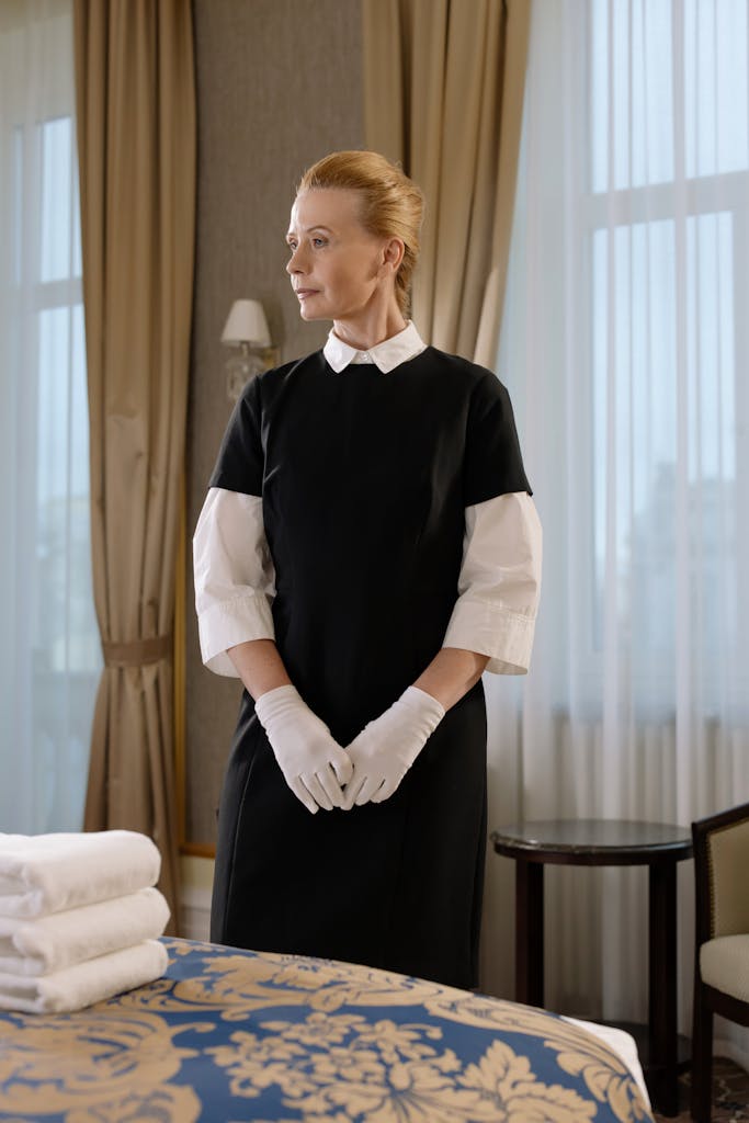 St. Augustine 12 Chambermaid in uniform standing in hotel room with folded linens, exuding professionalism.