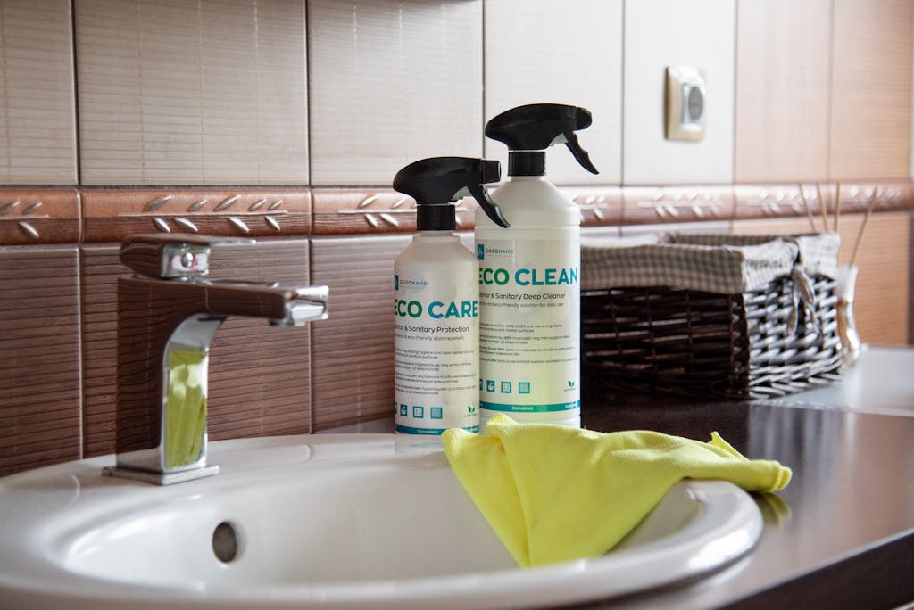 St. Augustine 25 Eco-friendly cleaning products displayed on a bathroom sink with tiles and a basket.