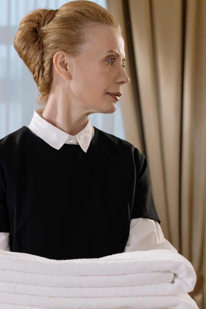 St. Augustine 15 Elegant housekeeper in uniform holding fresh towels in a well-lit hotel room.