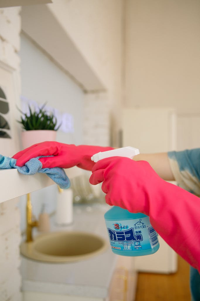 St. Augustine 7 Person using spray bottle and cloth for cleaning a kitchen shelf, ensuring hygiene and cleanliness.