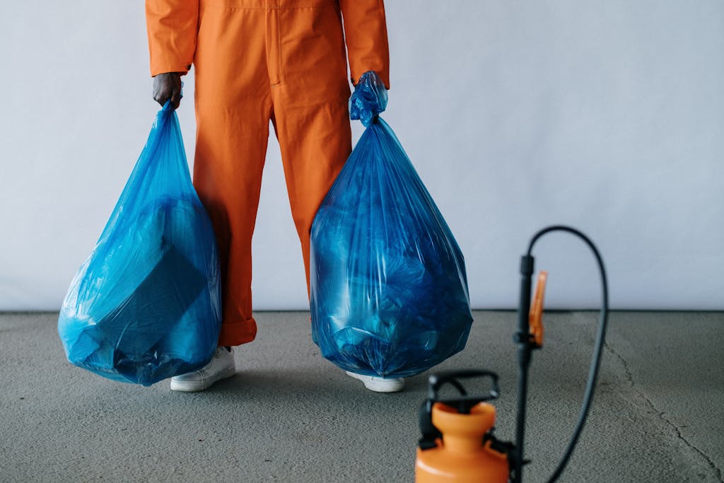 St. Augustine 19 Sanitation worker in orange overalls holding blue trash bags indoors for waste management.