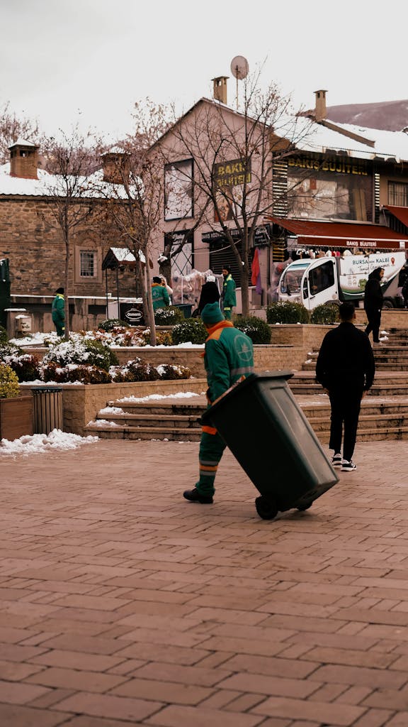 Sanitation workers in winter attire cleaning a cobblestone street lined with buildings.