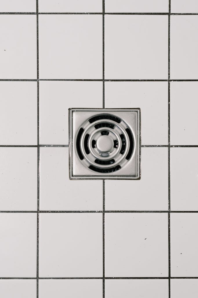 St. Augustine 22 Top view of white ceramic tile floor with stainless steel square shaped cover of drain in contemporary shower
